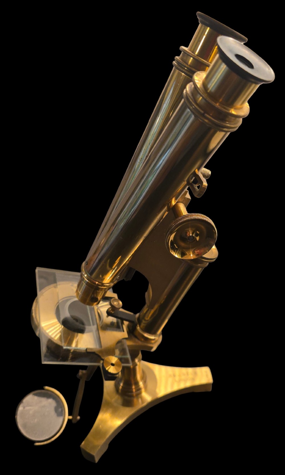 A Victorian lacquered brass binocular microscope featuring dual body tubes, knurled adjusting wheels, a stage plate, and a solid brass tripod foot.