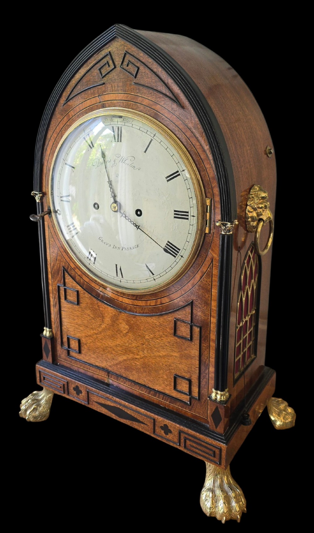 A Georgian mahogany lancet-top bracket clock featuring ebonised inlay, brass lion mask side handles, and decorative brass claw feet. View VII