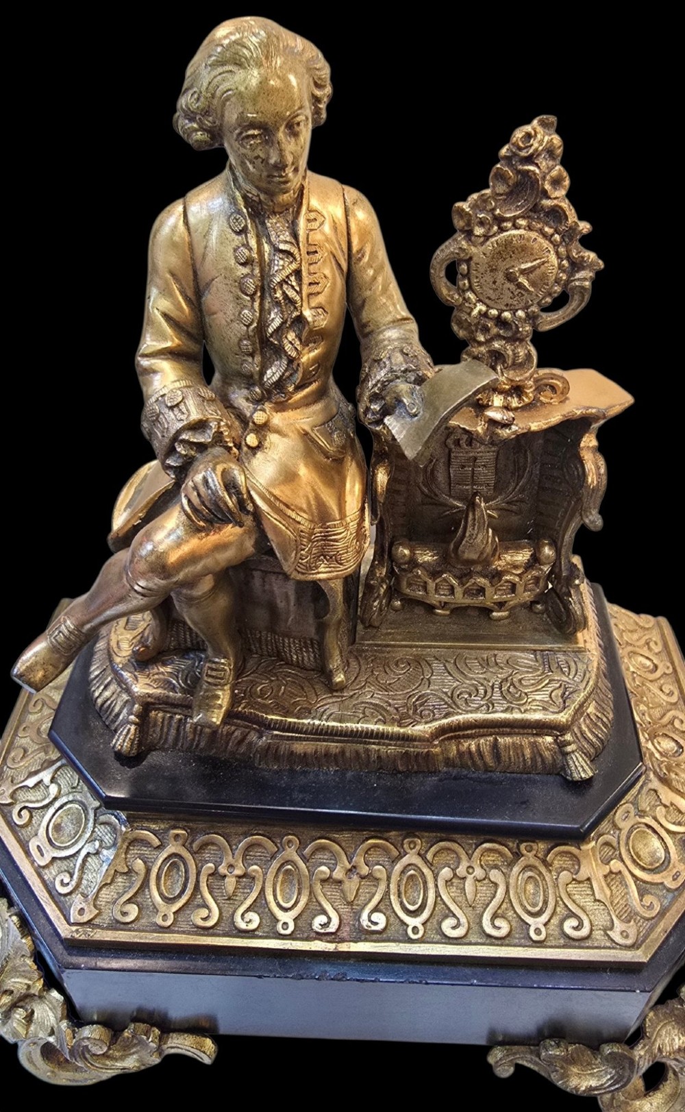 A 19th-century French gilt bronze sculpture depicting a seated gentleman in historic dress holding a quill, supported by an ornate black base with metallic scroll feet. View II