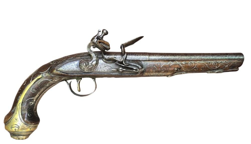 An early 19th-century Ottoman Balkan flintlock holster pistol featuring a dark wood stock inlaid with silver wire scrollwork and a cast brass pommel.