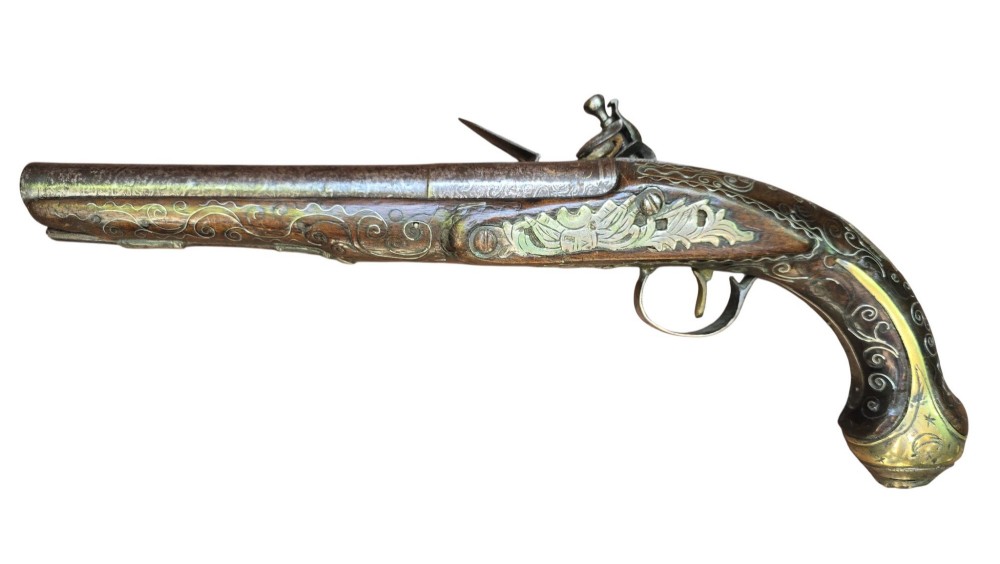 An early 19th-century Ottoman Balkan flintlock holster pistol featuring a dark wood stock inlaid with silver wire scrollwork and a cast brass pommel. View V
