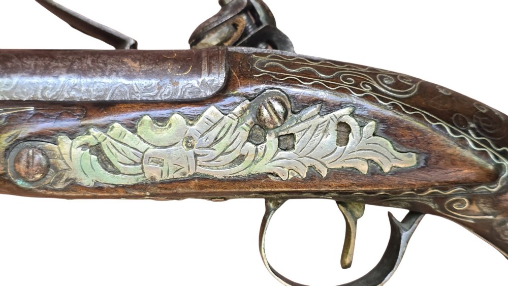 An early 19th-century Ottoman Balkan flintlock holster pistol featuring a dark wood stock inlaid with silver wire scrollwork and a cast brass pommel. View VI