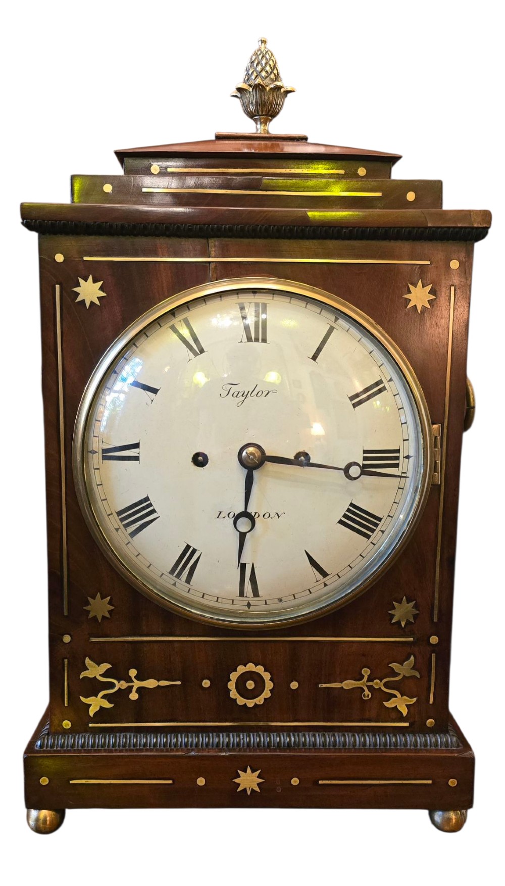 A Georgian mahogany bracket clock featuring brass star and floral motifs, a pineapple finial, brass ball feet, and a white dial marked Taylor London with Roman numerals.
