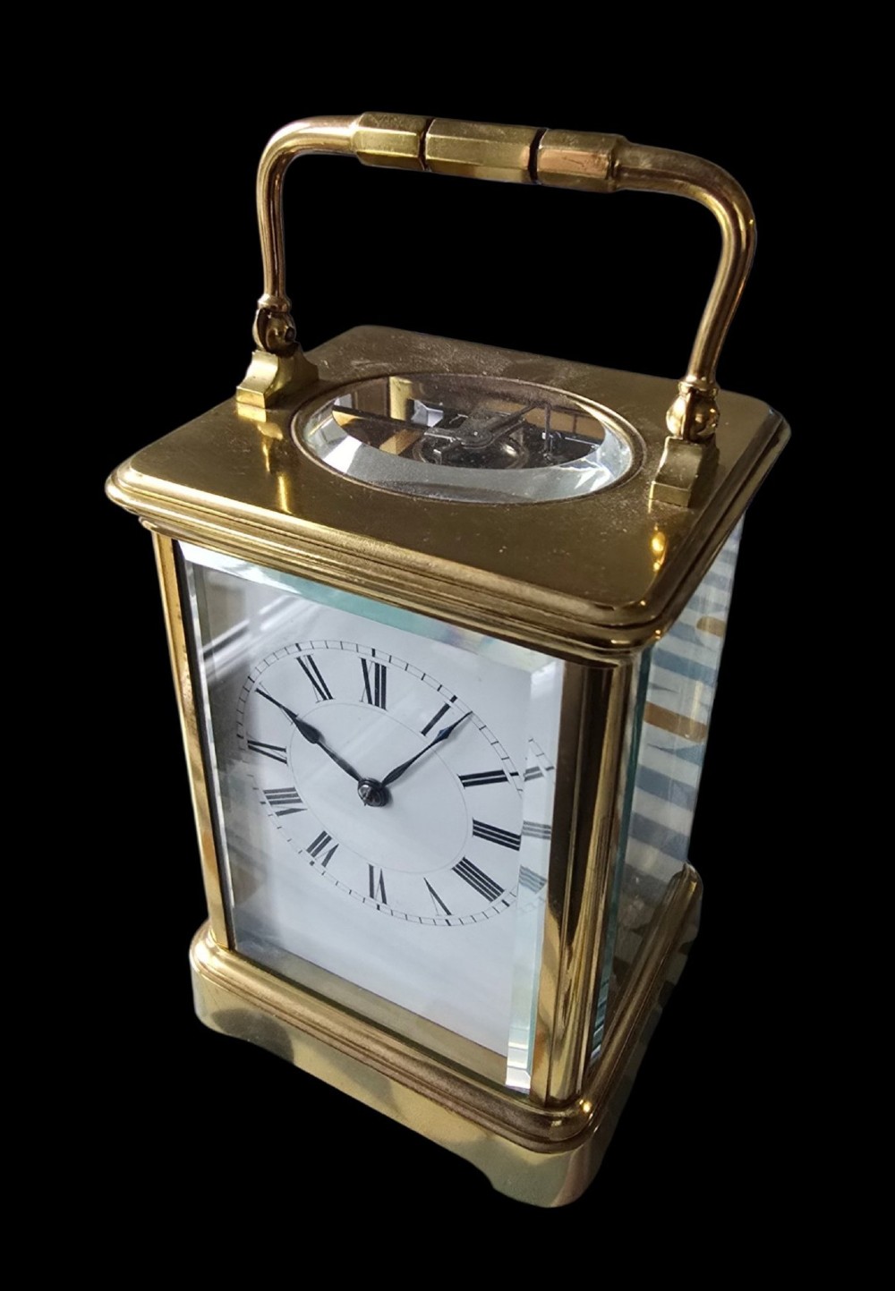 A rectangular French gilt-brass carriage clock featuring bevelled glass panels, a white enamel dial with Roman numerals, and a hinged top handle.