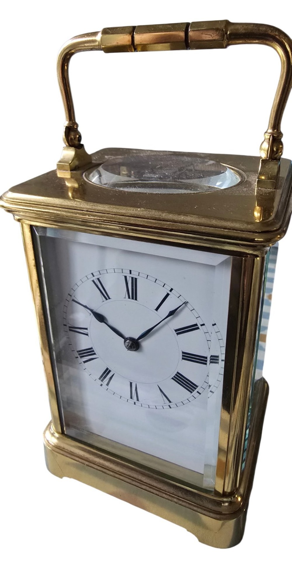 A rectangular French gilt-brass carriage clock featuring bevelled glass panels, a white enamel dial with Roman numerals, and a hinged top handle. View III