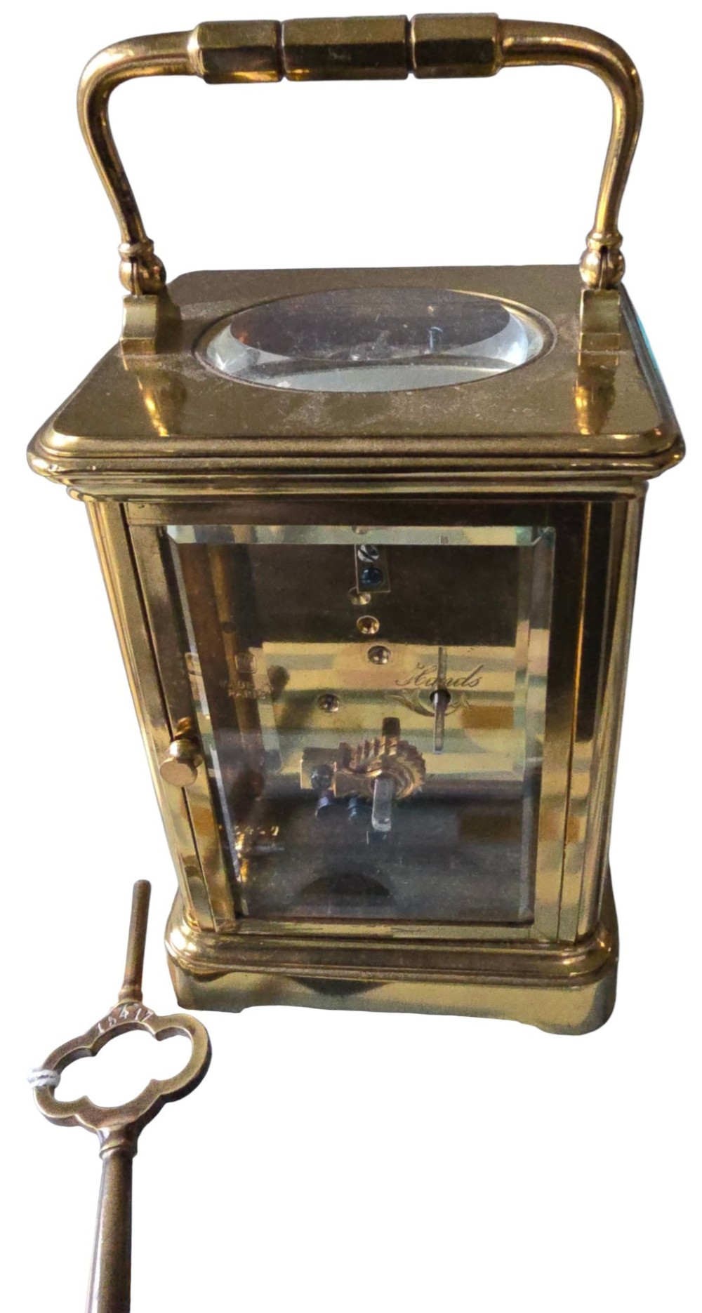 A rectangular French gilt-brass carriage clock featuring bevelled glass panels, a white enamel dial with Roman numerals, and a hinged top handle. View V