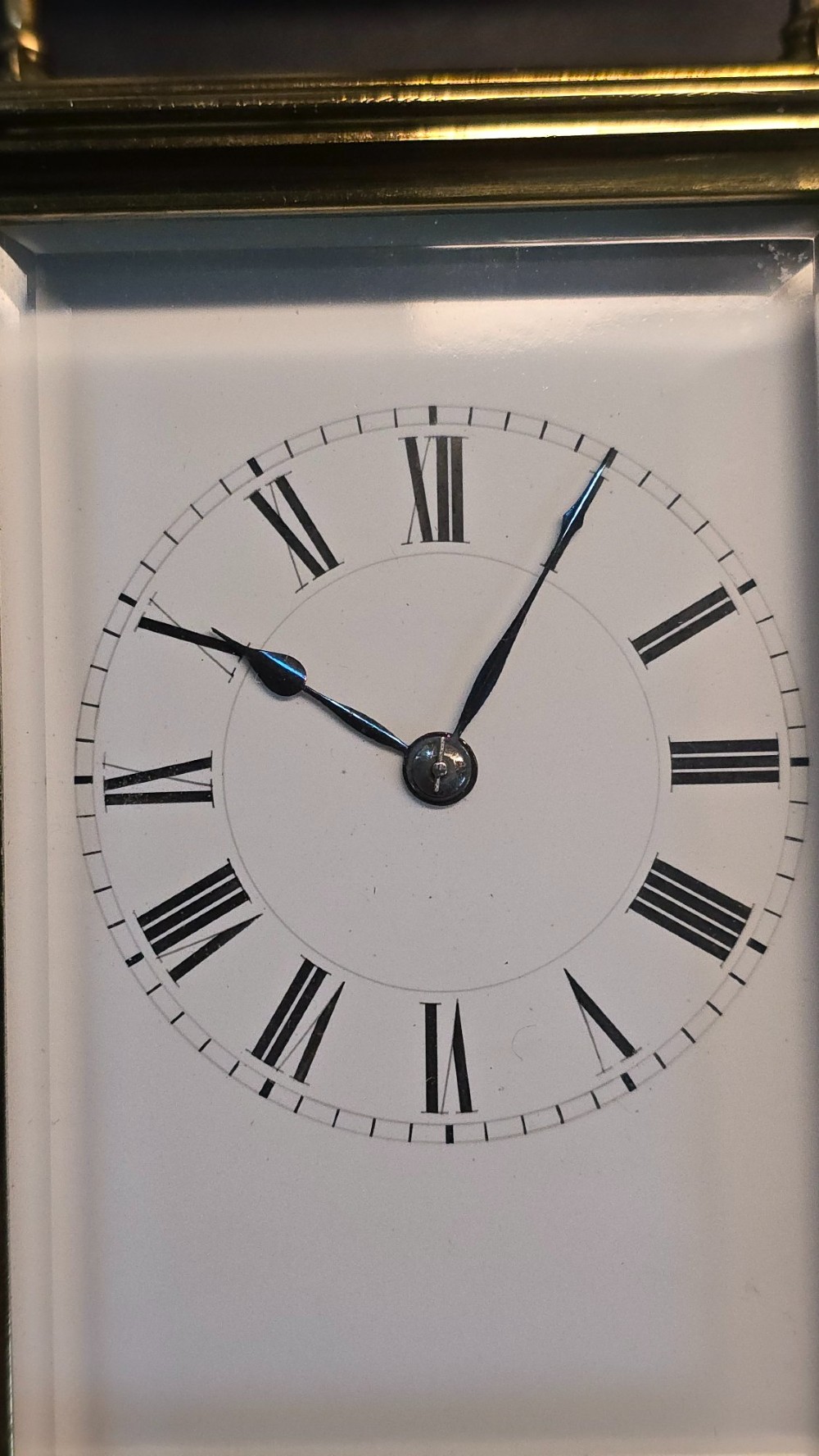 A rectangular French gilt-brass carriage clock featuring bevelled glass panels, a white enamel dial with Roman numerals, and a hinged top handle. View VII
