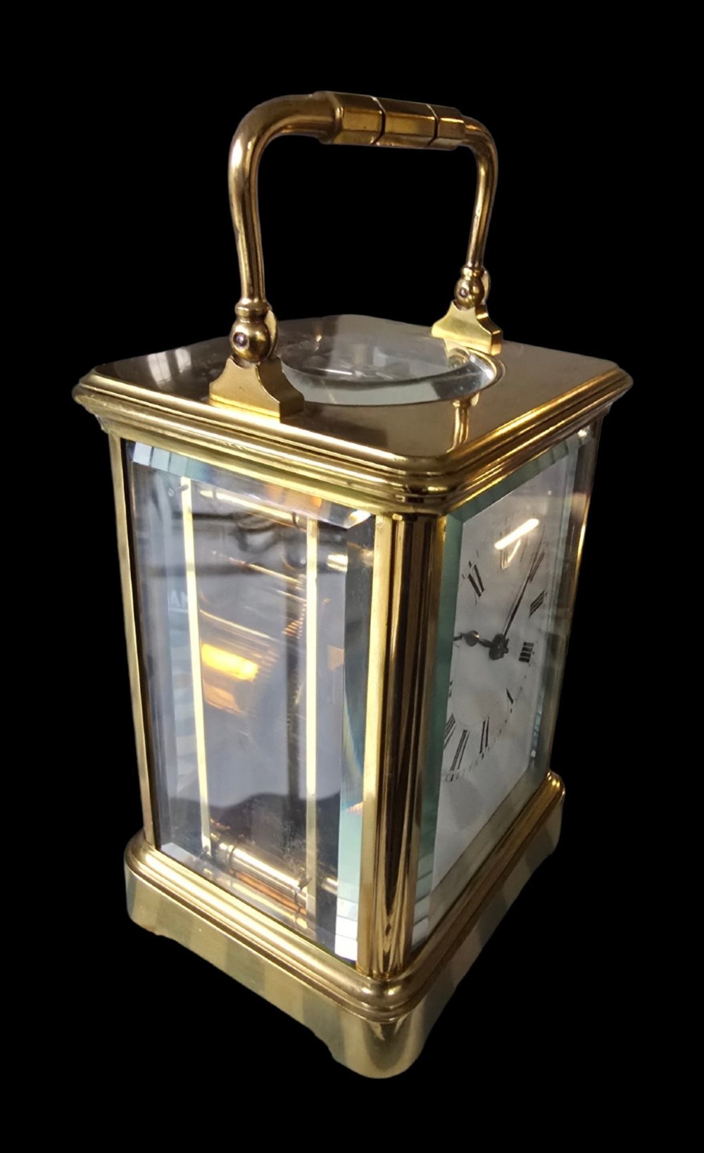 A rectangular French gilt-brass carriage clock featuring bevelled glass panels, a white enamel dial with Roman numerals, and a hinged top handle. View XI