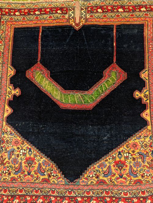 fig 1. An antique hand-knotted Persian Senneh saddle cover featuring a dark navy field with a central saddle notch, floral spandrels, and multi-banded red patterned borders.