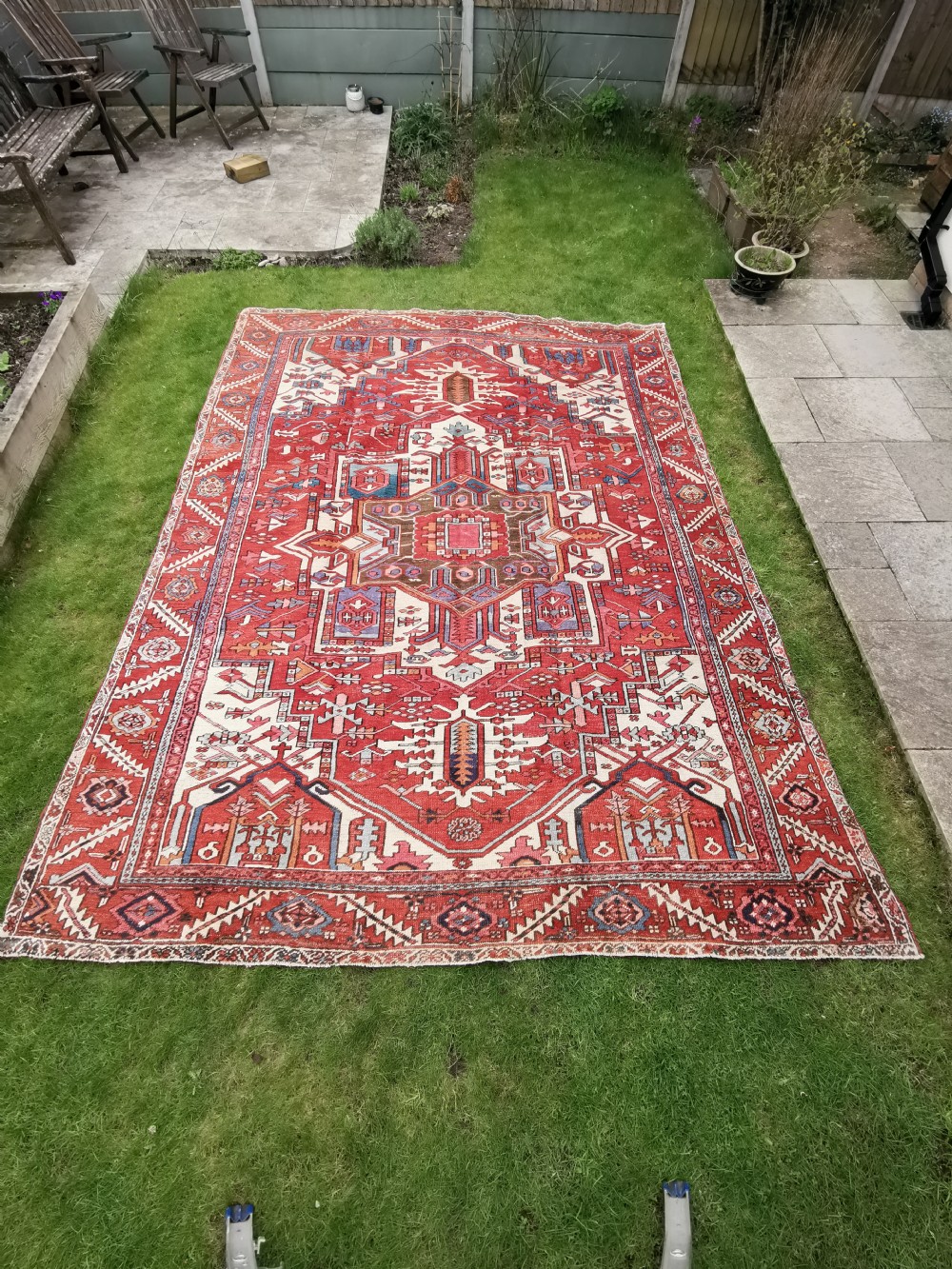 A rectangular Persian Heriz hand-knotted wool carpet featuring a red geometric field with a central star medallion, cream corner spandrels, and multi-banded borders.