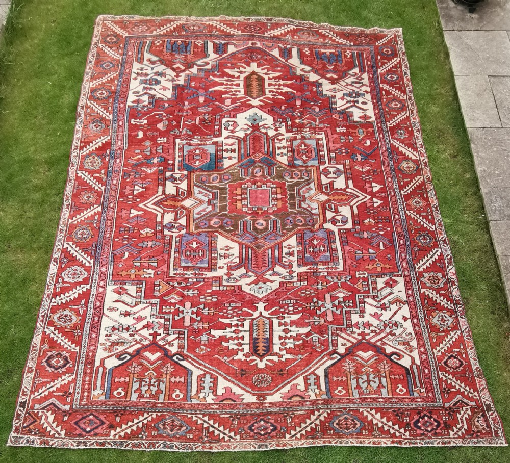 A rectangular Persian Heriz hand-knotted wool carpet featuring a red geometric field with a central star medallion, cream corner spandrels, and multi-banded borders. View III