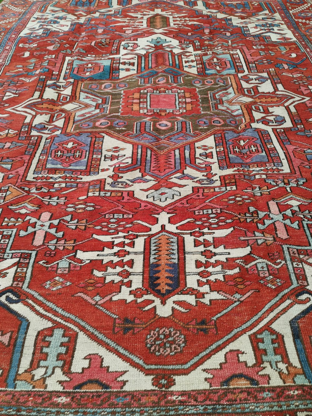A rectangular Persian Heriz hand-knotted wool carpet featuring a red geometric field with a central star medallion, cream corner spandrels, and multi-banded borders. View IV