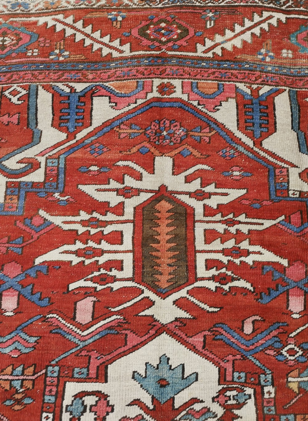 A rectangular Persian Heriz hand-knotted wool carpet featuring a red geometric field with a central star medallion, cream corner spandrels, and multi-banded borders. View VI