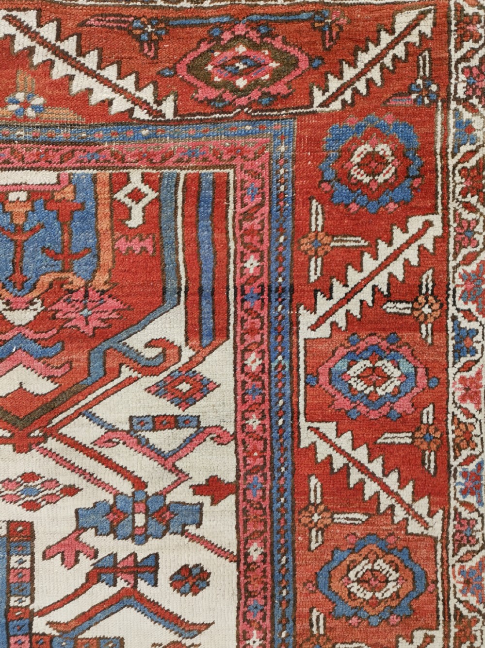 A rectangular Persian Heriz hand-knotted wool carpet featuring a red geometric field with a central star medallion, cream corner spandrels, and multi-banded borders. View VII
