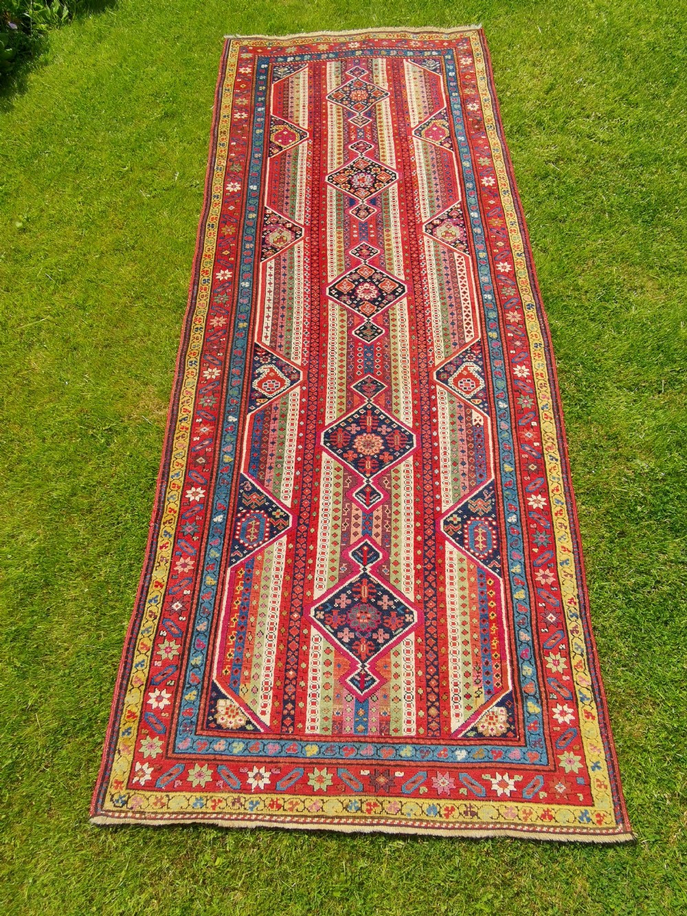 A long hand-knotted antique Caucasian Karabagh wool runner rug featuring central diamond medallions and geometric borders in red, blue, and yellow.