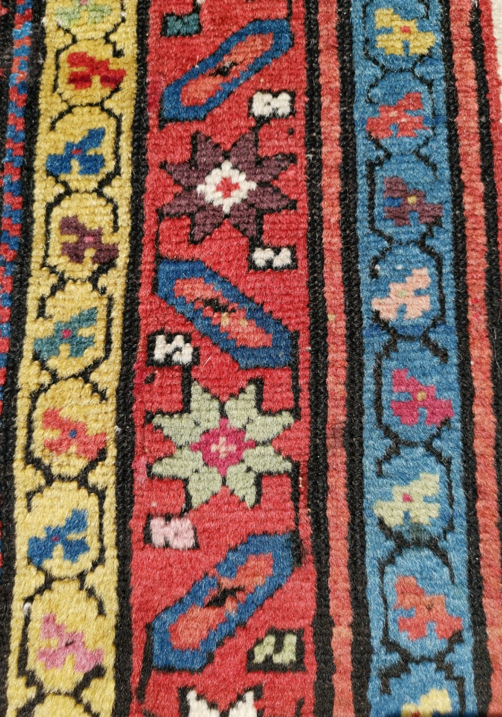 A long hand-knotted antique Caucasian Karabagh wool runner rug featuring central diamond medallions and geometric borders in red, blue, and yellow. View V