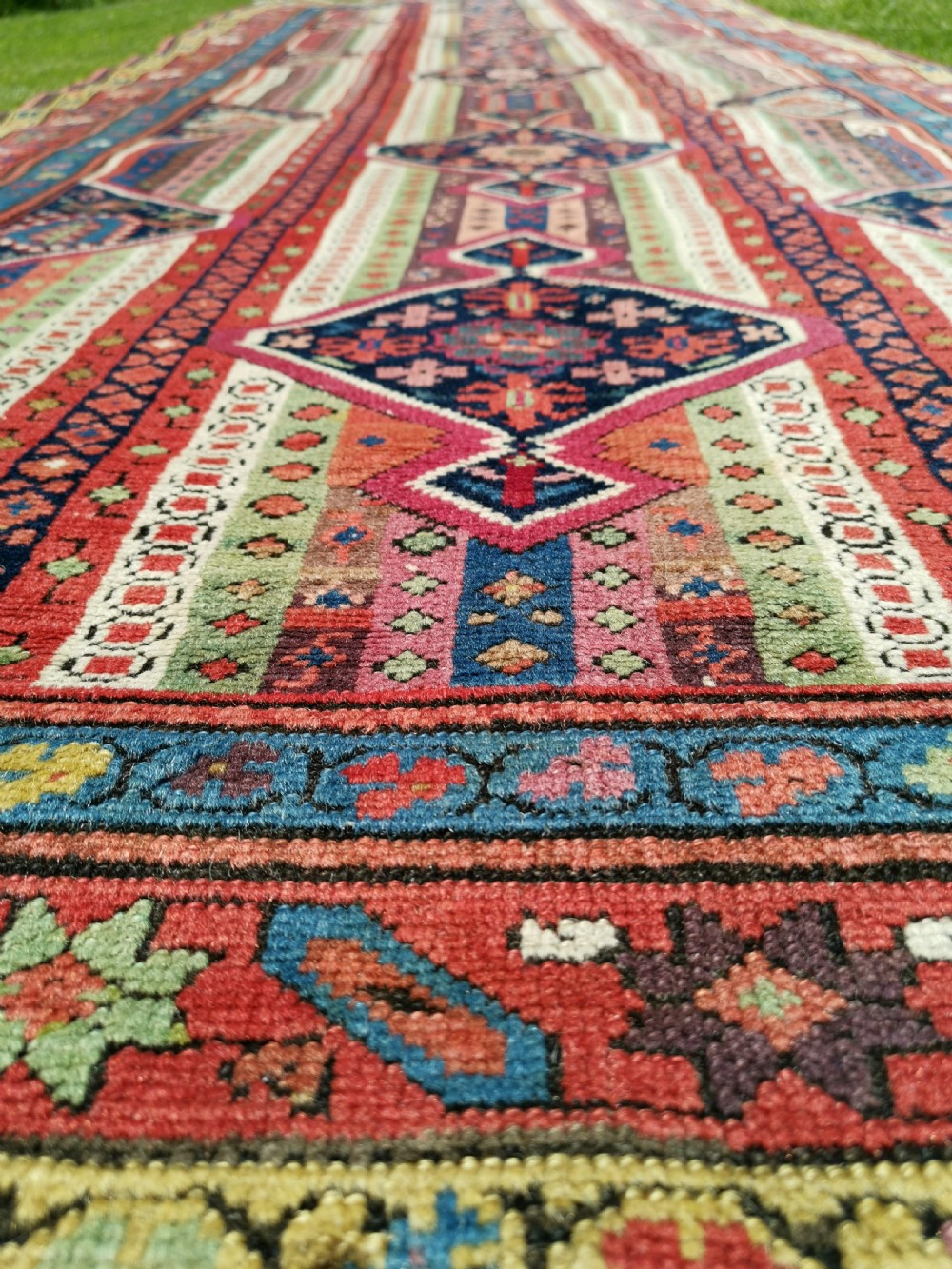 A long hand-knotted antique Caucasian Karabagh wool runner rug featuring central diamond medallions and geometric borders in red, blue, and yellow. View VI