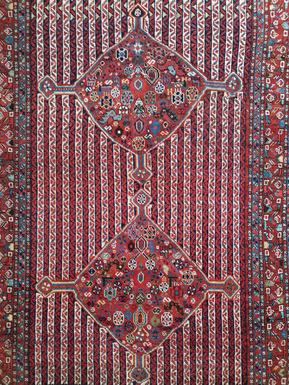 A rectangular hand-knotted antique Khamseh rug featuring vertical striped field patterns and two diamond-shaped medallions in deep red, indigo, and ivory wool. View II