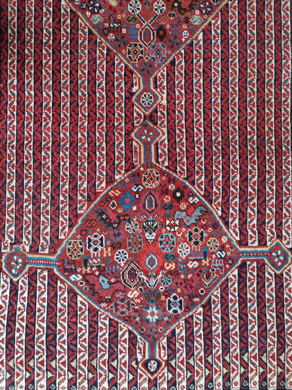 A rectangular hand-knotted antique Khamseh rug featuring vertical striped field patterns and two diamond-shaped medallions in deep red, indigo, and ivory wool. View III