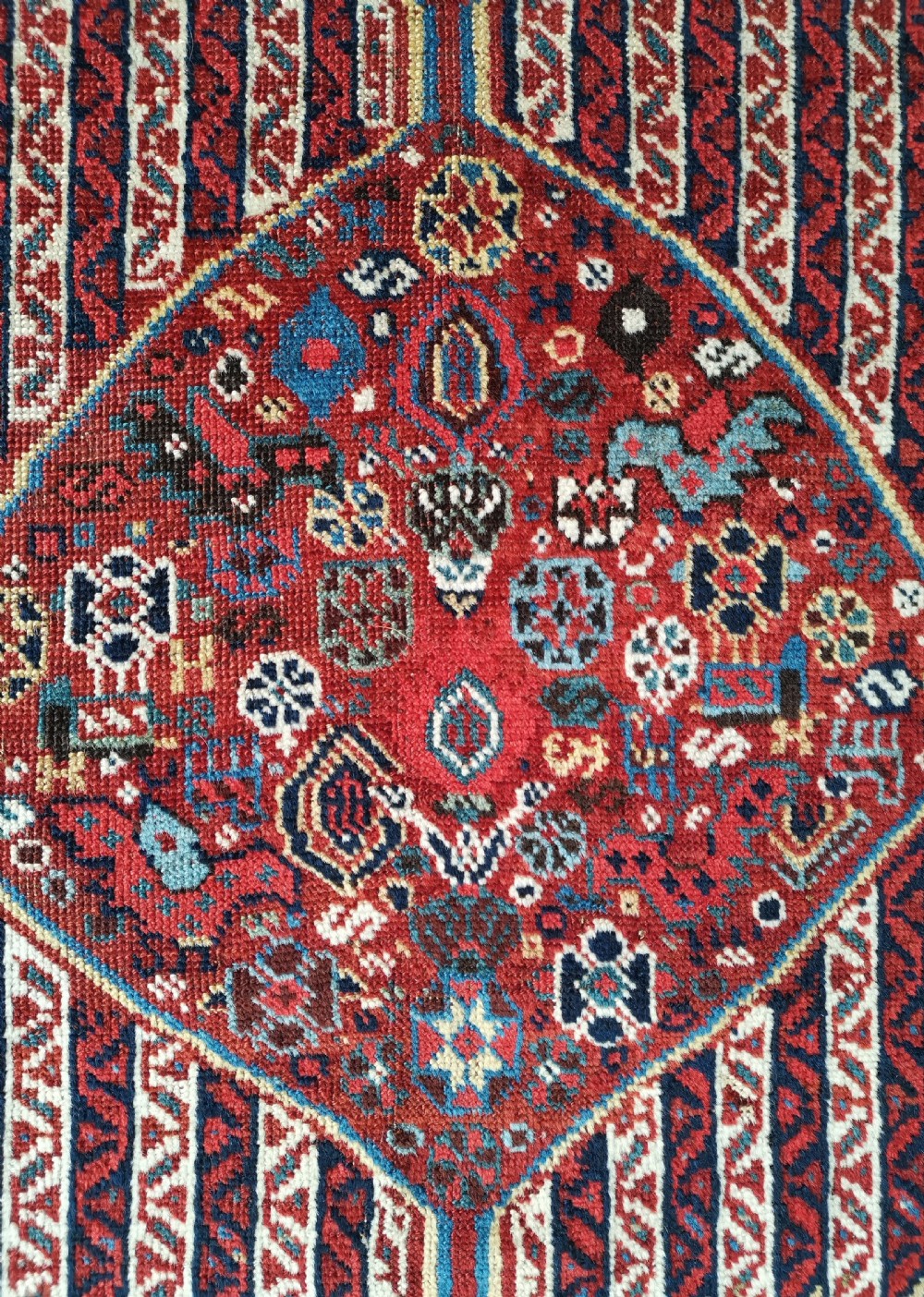 A rectangular hand-knotted antique Khamseh rug featuring vertical striped field patterns and two diamond-shaped medallions in deep red, indigo, and ivory wool. View IV