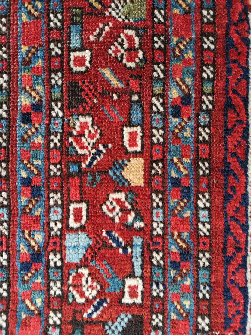 A rectangular hand-knotted antique Khamseh rug featuring vertical striped field patterns and two diamond-shaped medallions in deep red, indigo, and ivory wool. View VI