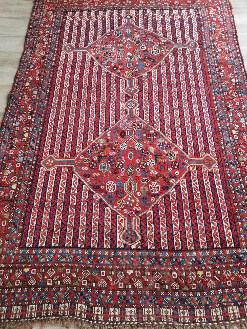 A rectangular hand-knotted antique Khamseh rug featuring vertical striped field patterns and two diamond-shaped medallions in deep red, indigo, and ivory wool. View VII