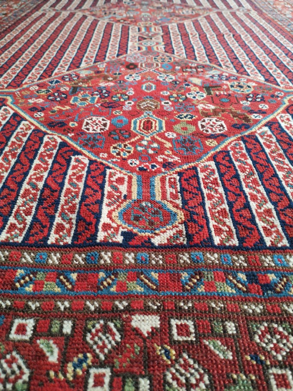 A rectangular hand-knotted antique Khamseh rug featuring vertical striped field patterns and two diamond-shaped medallions in deep red, indigo, and ivory wool. View VIII