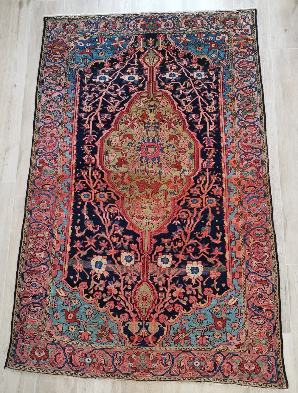 A hand-knotted antique Persian Mishan Malayer wool rug with a navy blue field, central olive medallion, and rose pink floral borders.