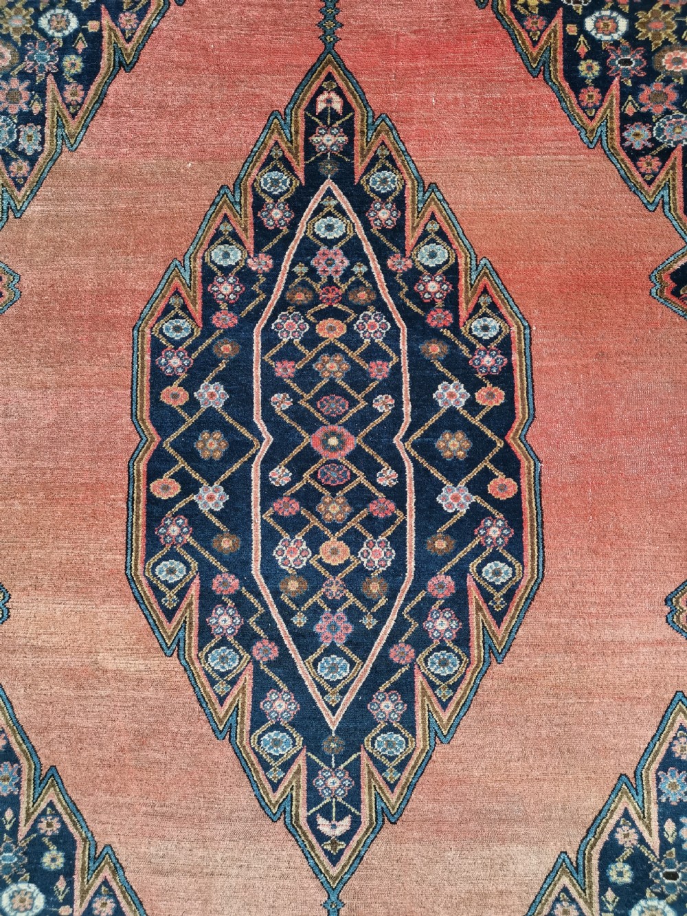 An antique Persian Malayer wool rug featuring a terracotta field, a central navy blue diamond medallion, and detailed geometric floral borders. View II