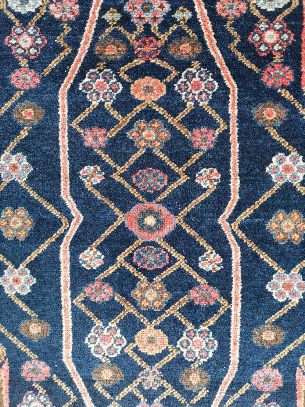 An antique Persian Malayer wool rug featuring a terracotta field, a central navy blue diamond medallion, and detailed geometric floral borders. View III