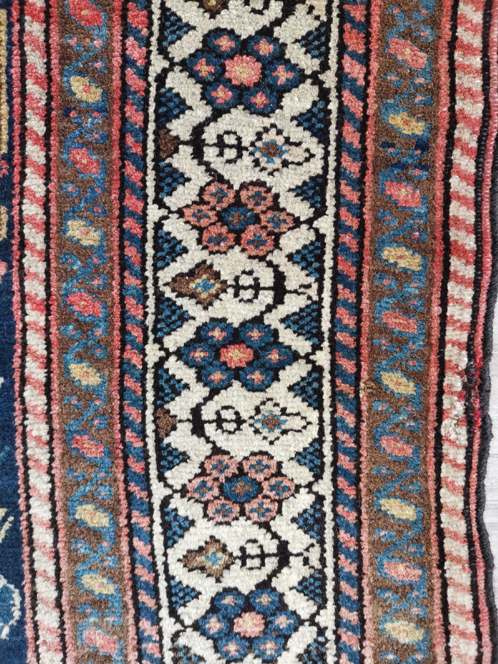 An antique Persian Malayer wool rug featuring a terracotta field, a central navy blue diamond medallion, and detailed geometric floral borders. View V
