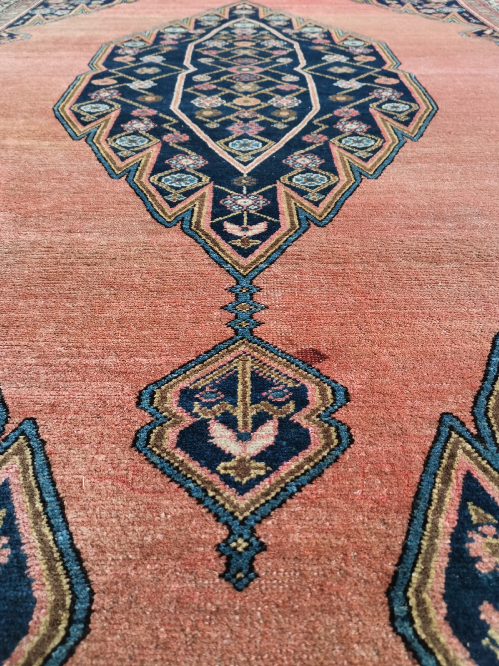 An antique Persian Malayer wool rug featuring a terracotta field, a central navy blue diamond medallion, and detailed geometric floral borders. View VI