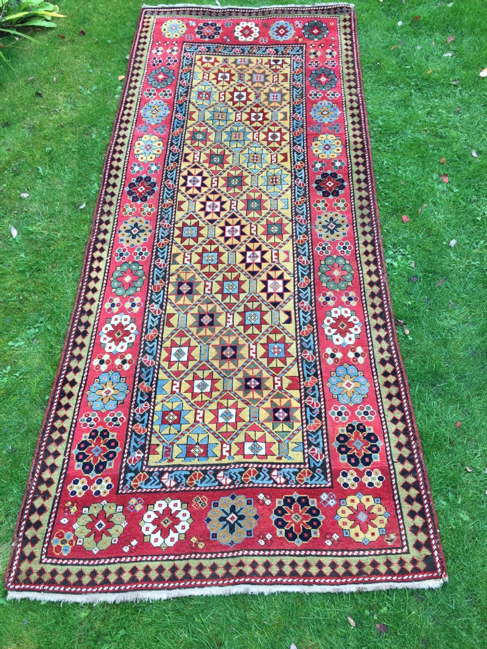 An antique hand-knotted Caucasian Gendje wool runner rug featuring a yellow central field with star motifs surrounded by a wide red border with rosettes.
