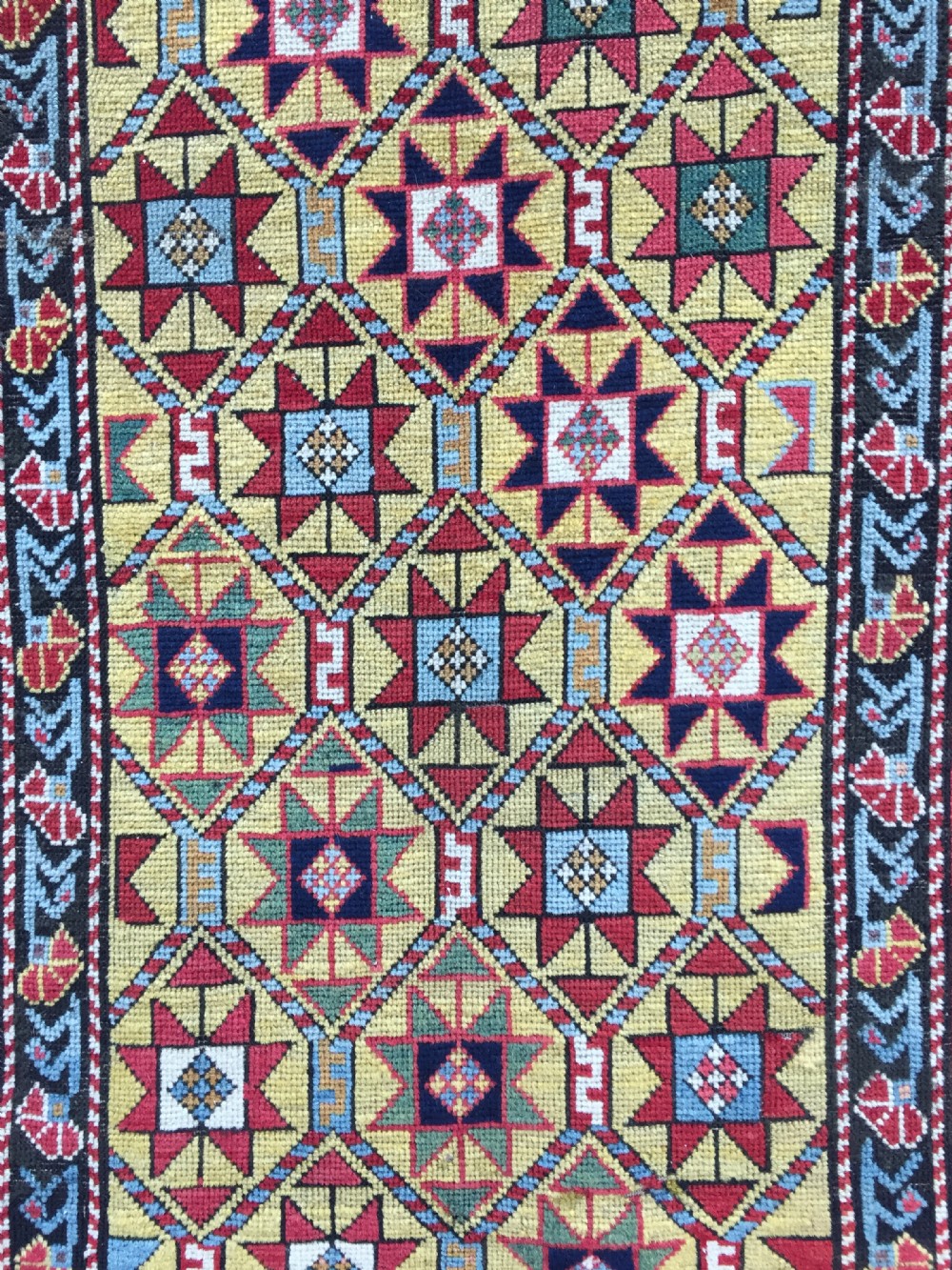 An antique hand-knotted Caucasian Gendje wool runner rug featuring a yellow central field with star motifs surrounded by a wide red border with rosettes. View VI