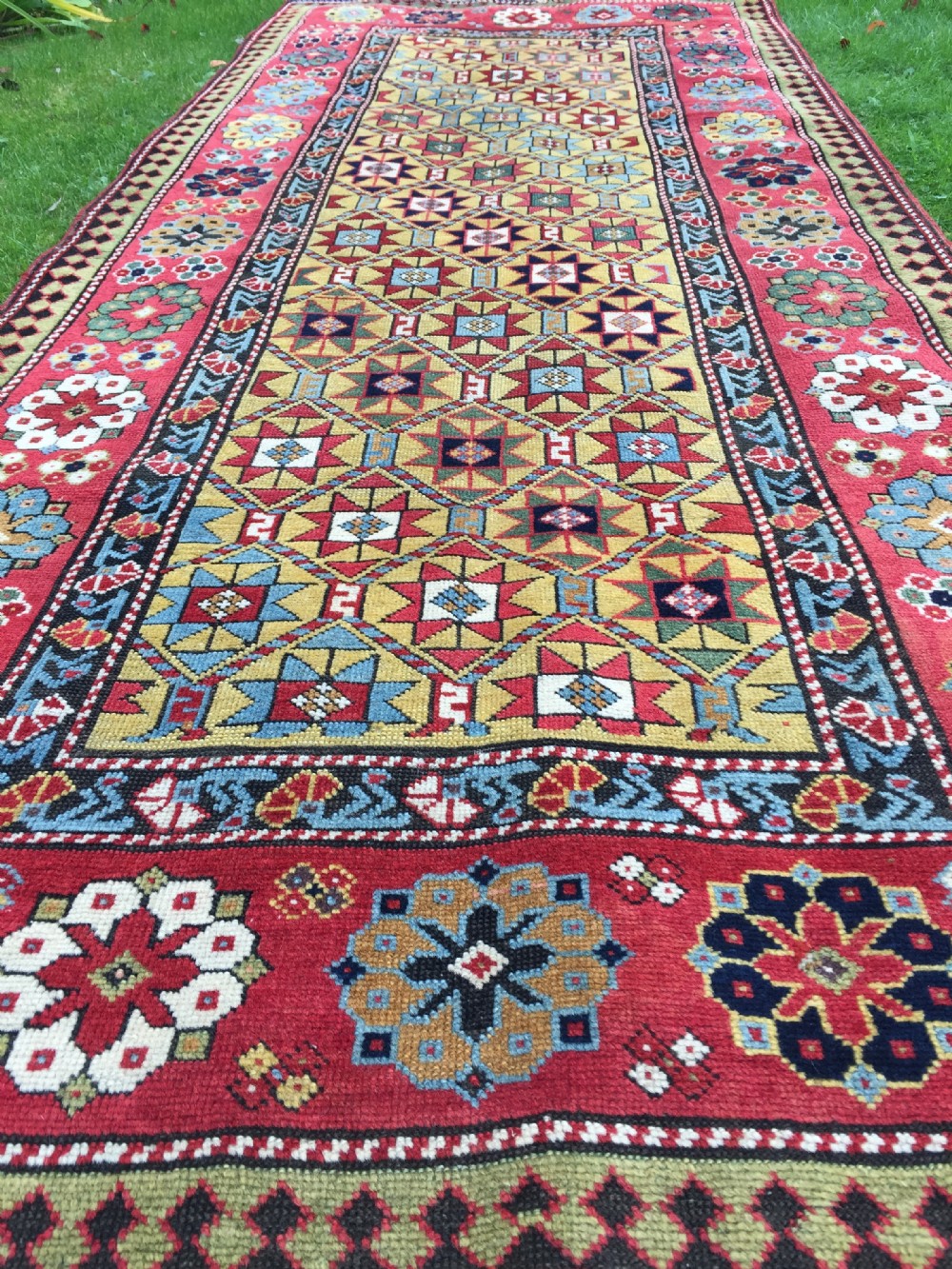 An antique hand-knotted Caucasian Gendje wool runner rug featuring a yellow central field with star motifs surrounded by a wide red border with rosettes. View VII