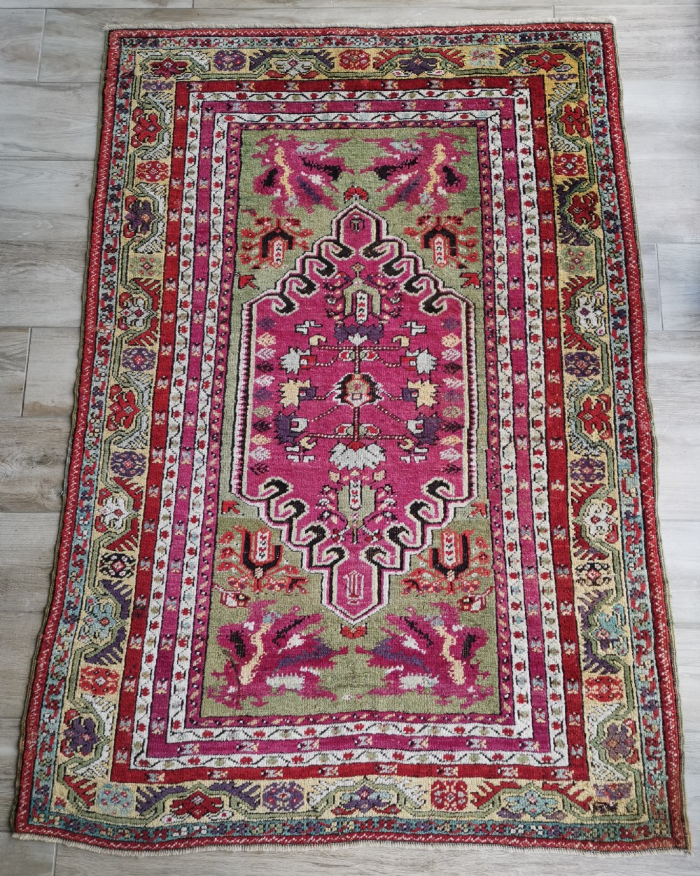 A hand-knotted Anatolian Kirsehir wool rug featuring a central magenta stepped medallion set within an olive green field and surrounded by multi-banded geometric borders.