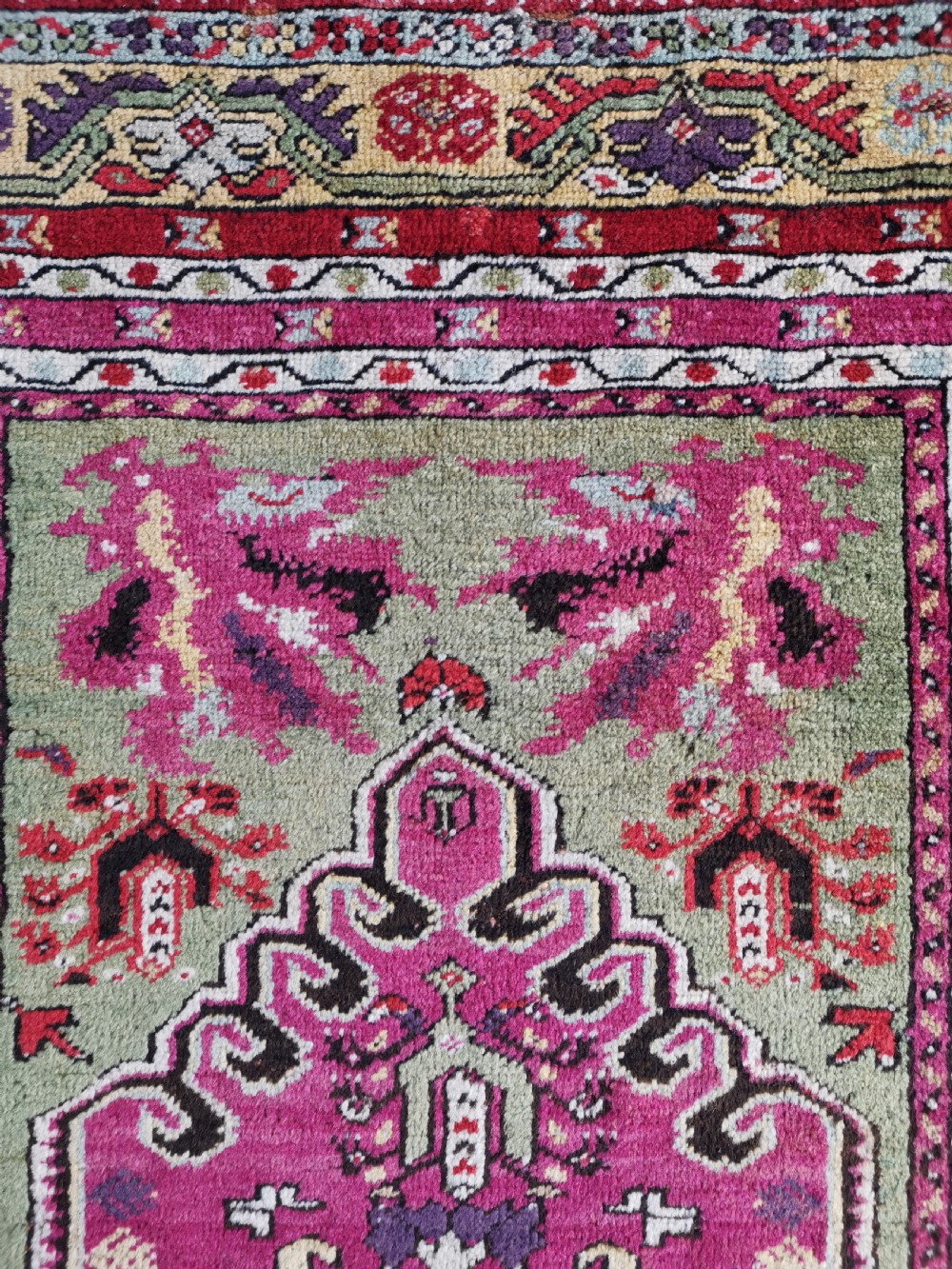A hand-knotted Anatolian Kirsehir wool rug featuring a central magenta stepped medallion set within an olive green field and surrounded by multi-banded geometric borders. View VII