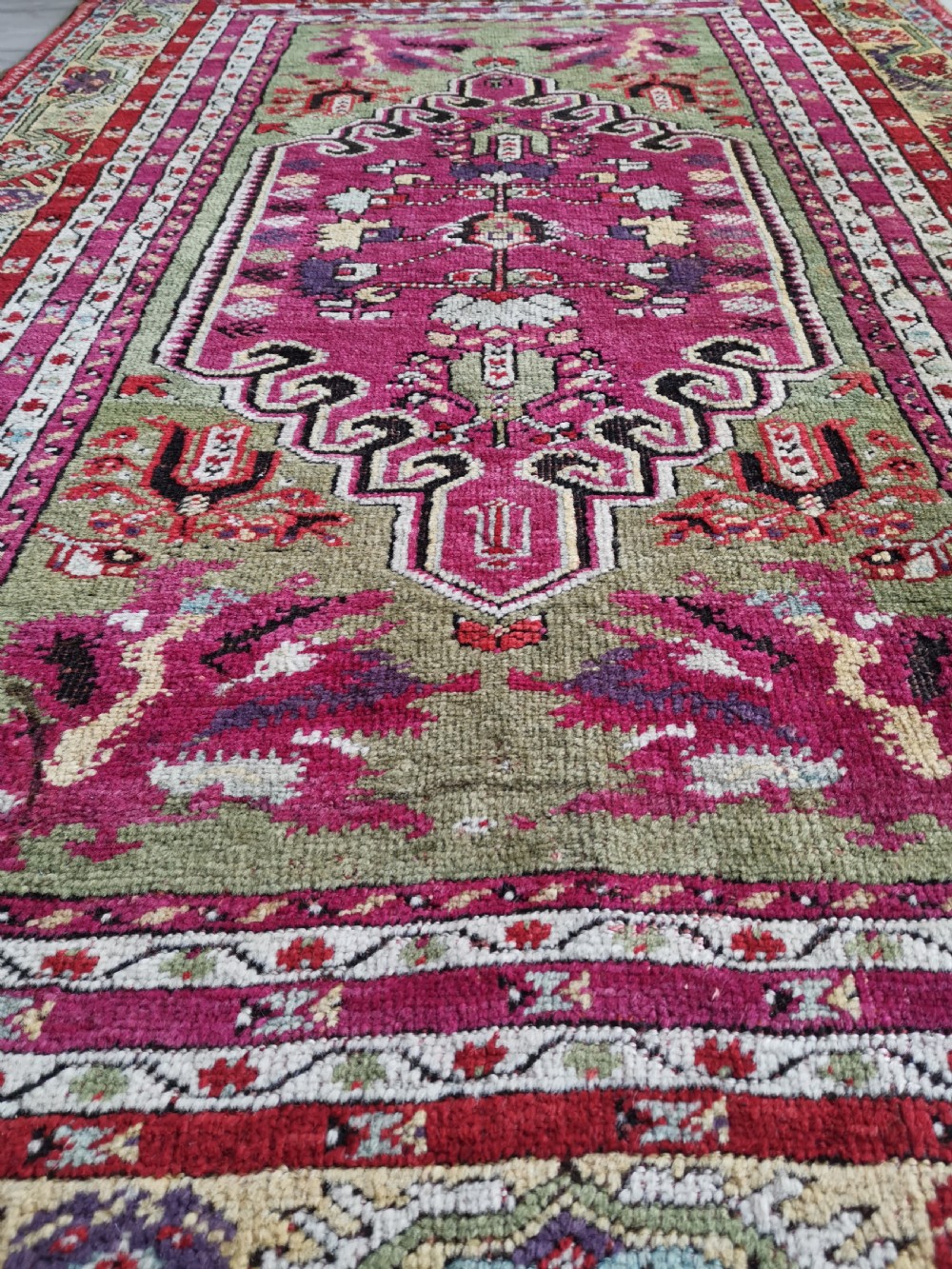 A hand-knotted Anatolian Kirsehir wool rug featuring a central magenta stepped medallion set within an olive green field and surrounded by multi-banded geometric borders. View VIII