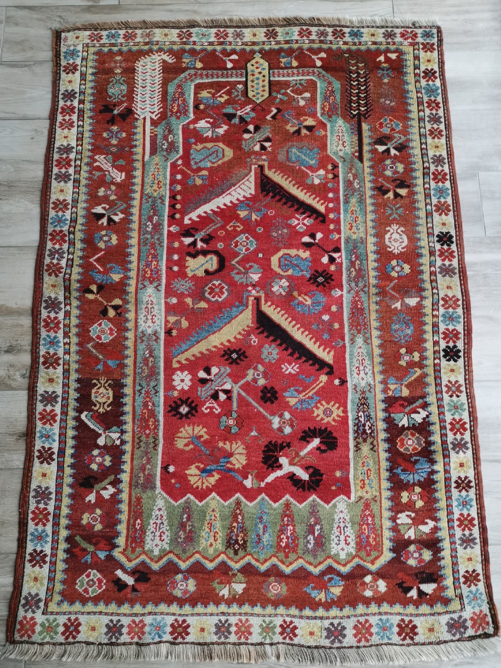 An antique hand-knotted Melas wool rug featuring a terracotta red central field with a stepped prayer arch motif and geometric multi-patterned borders.