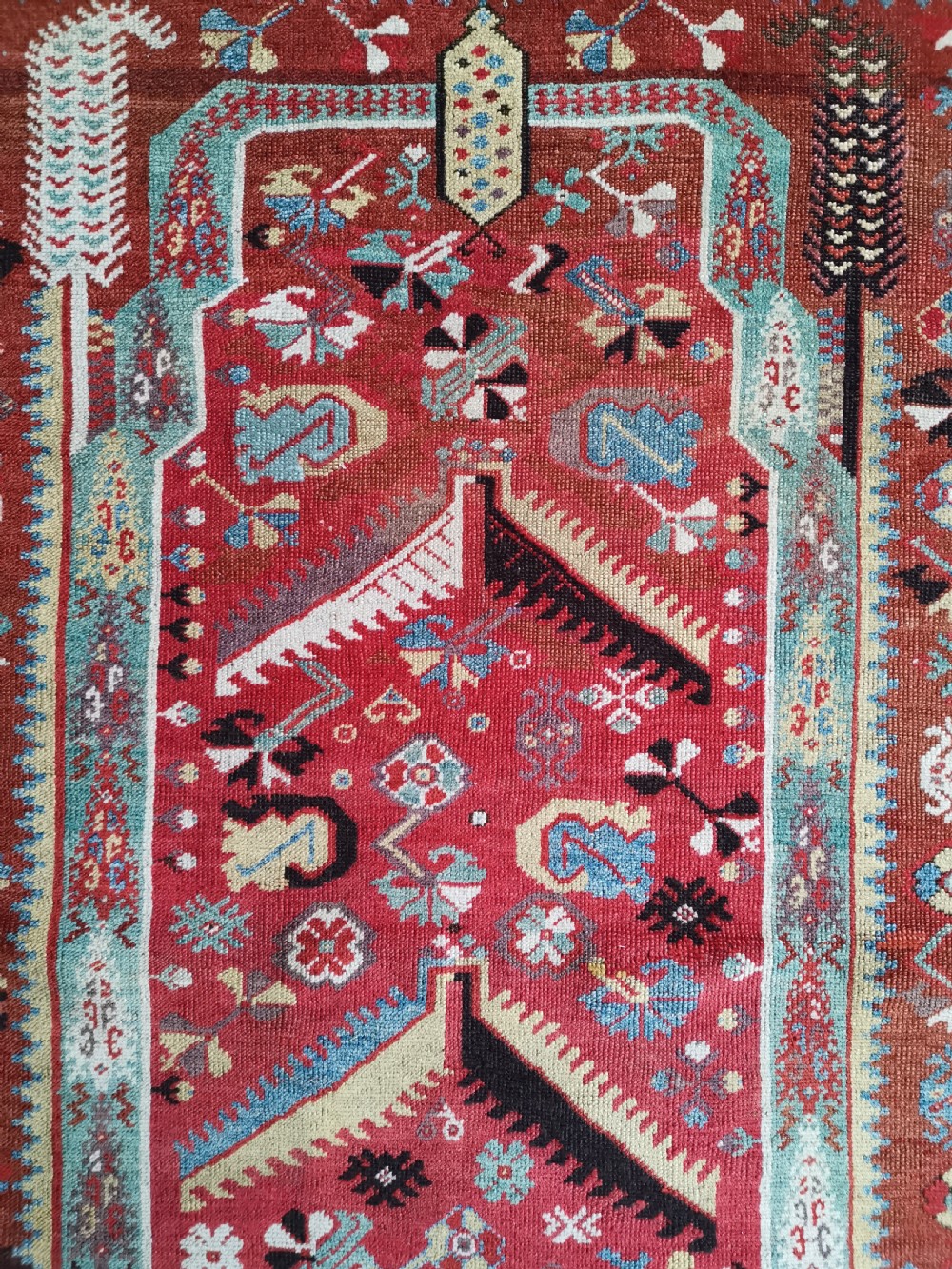 An antique hand-knotted Melas wool rug featuring a terracotta red central field with a stepped prayer arch motif and geometric multi-patterned borders. View II