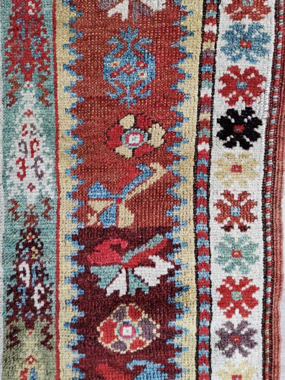 An antique hand-knotted Melas wool rug featuring a terracotta red central field with a stepped prayer arch motif and geometric multi-patterned borders. View III
