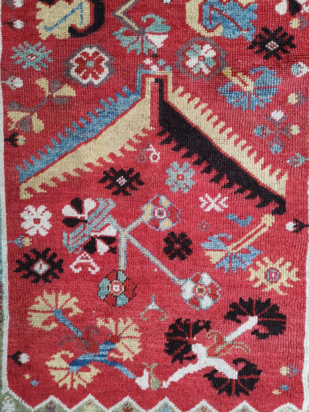 An antique hand-knotted Melas wool rug featuring a terracotta red central field with a stepped prayer arch motif and geometric multi-patterned borders. View V