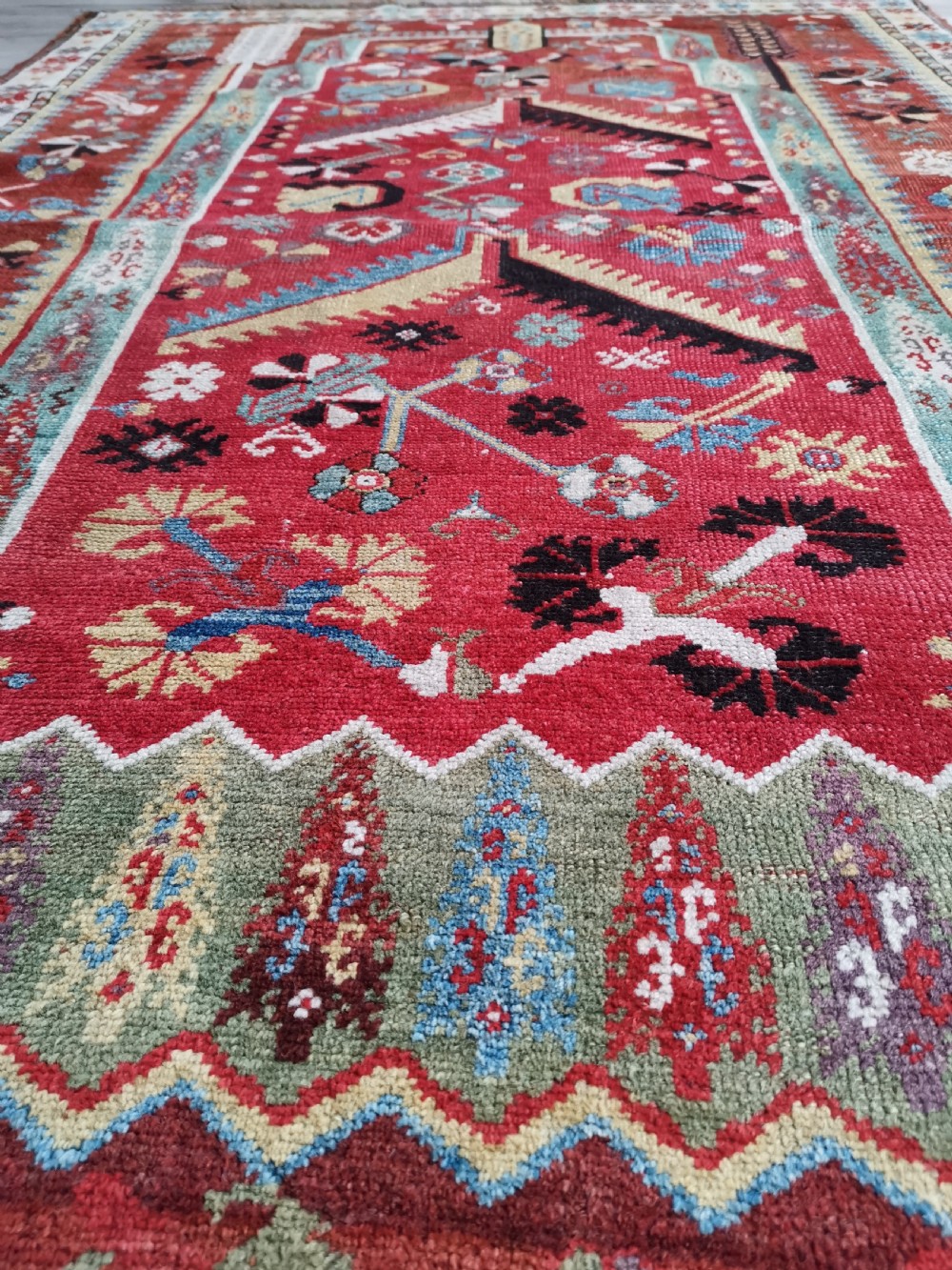 An antique hand-knotted Melas wool rug featuring a terracotta red central field with a stepped prayer arch motif and geometric multi-patterned borders. View VI