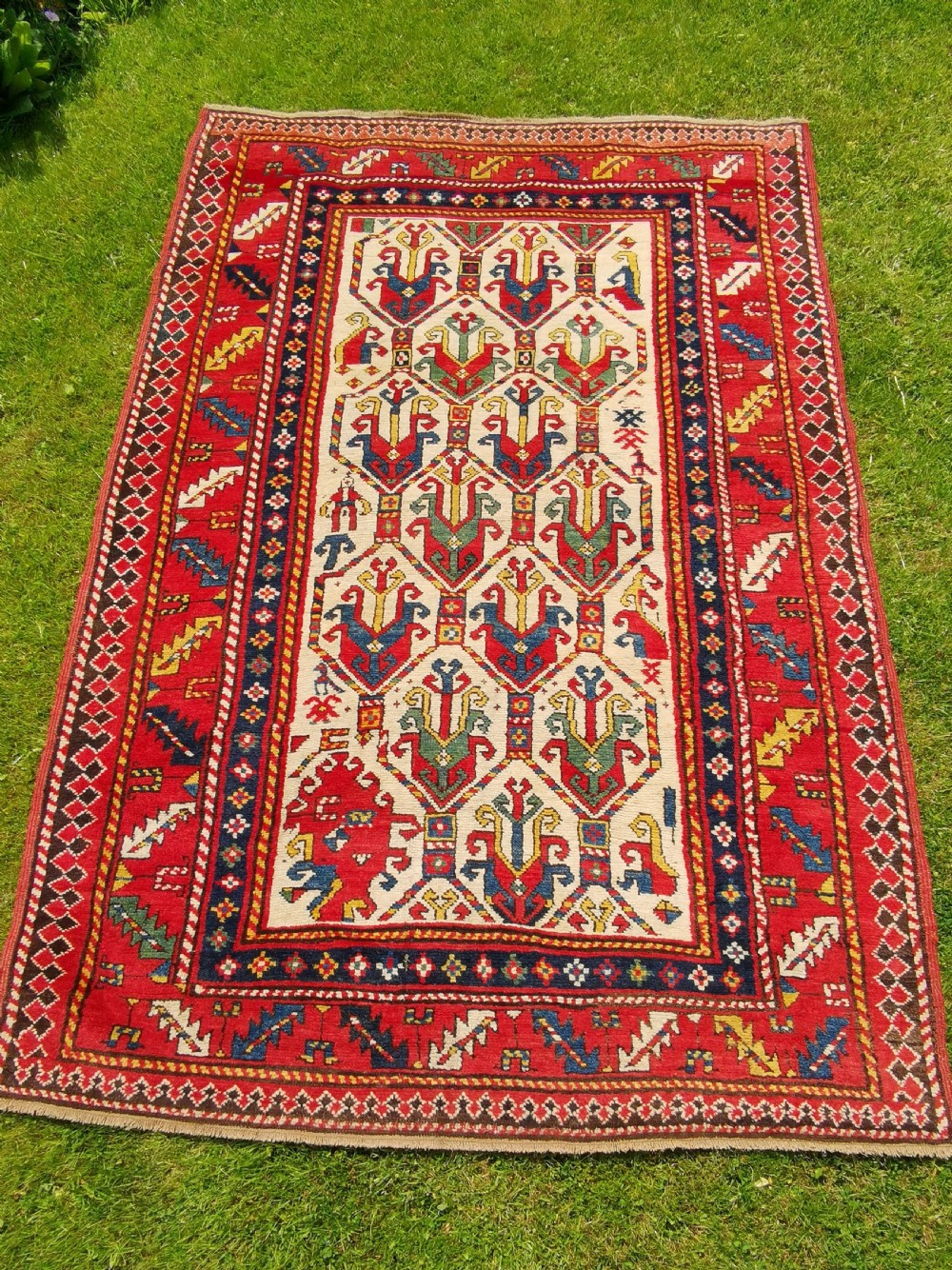 An antique hand-knotted Caucasian Gendje wool rug featuring an ivory central field with geometric lattice patterns framed by a wide red border.