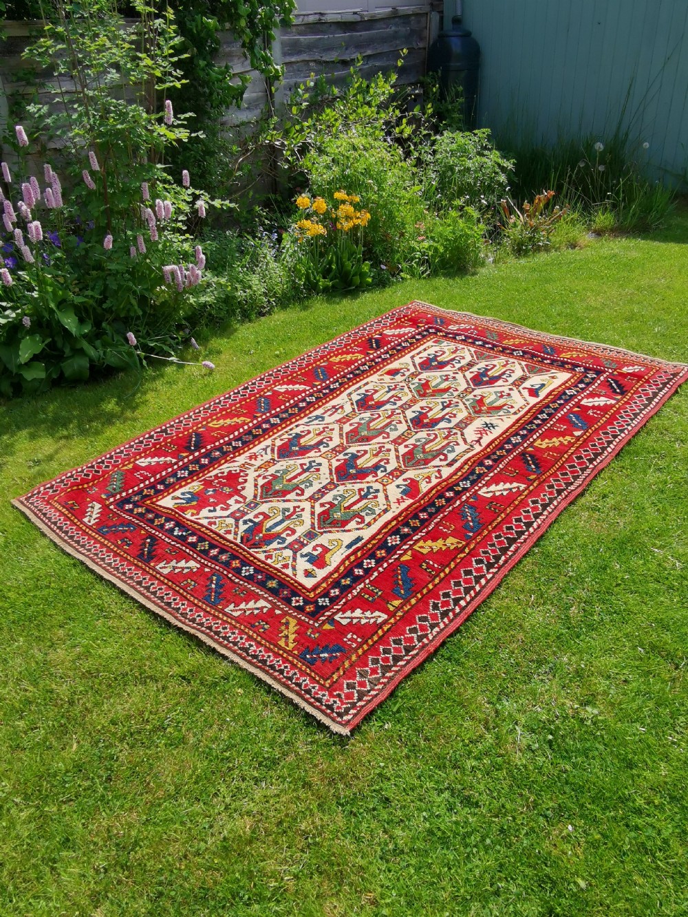 An antique hand-knotted Caucasian Gendje wool rug featuring an ivory central field with geometric lattice patterns framed by a wide red border. View II