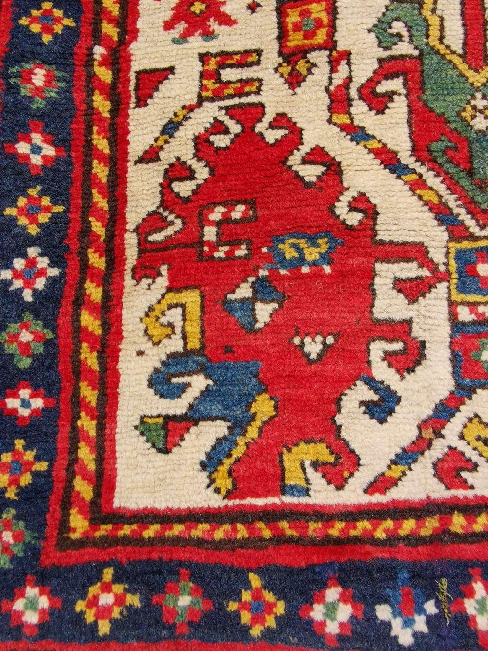An antique hand-knotted Caucasian Gendje wool rug featuring an ivory central field with geometric lattice patterns framed by a wide red border. View III