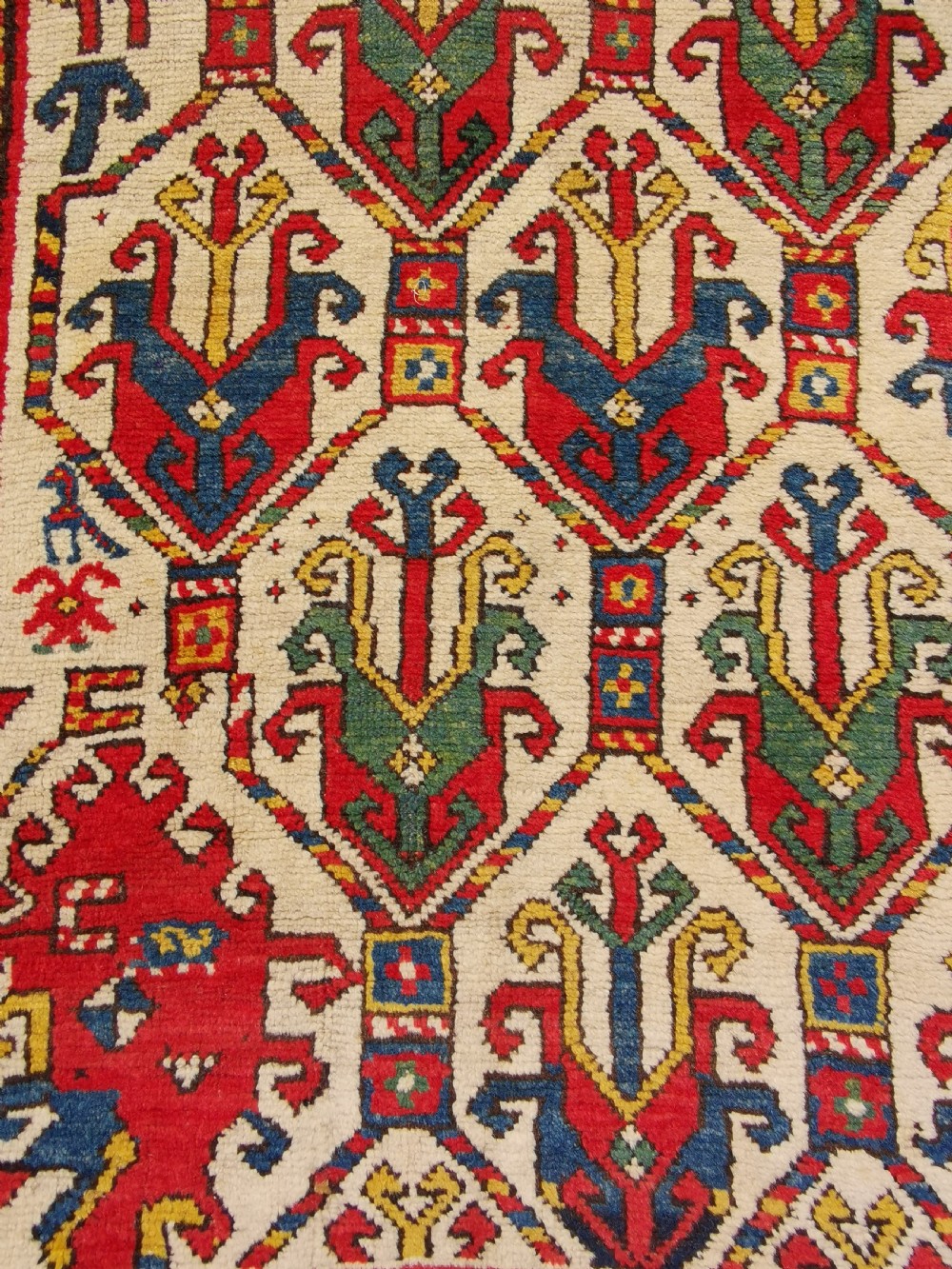 An antique hand-knotted Caucasian Gendje wool rug featuring an ivory central field with geometric lattice patterns framed by a wide red border. View IV