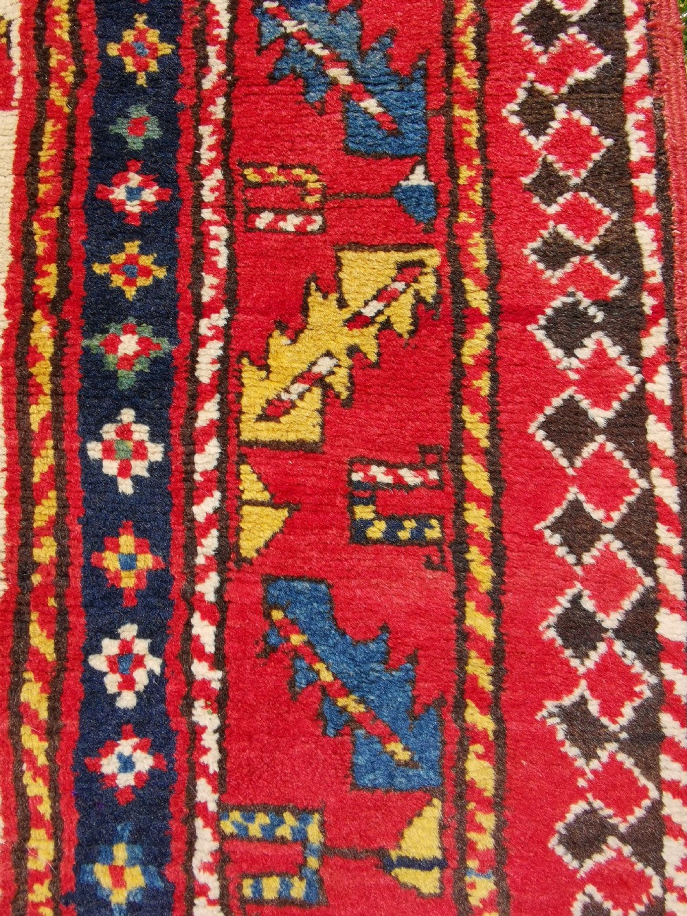 An antique hand-knotted Caucasian Gendje wool rug featuring an ivory central field with geometric lattice patterns framed by a wide red border. View V