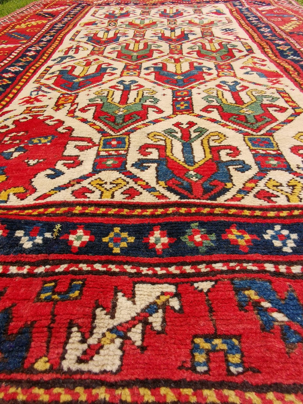 An antique hand-knotted Caucasian Gendje wool rug featuring an ivory central field with geometric lattice patterns framed by a wide red border. View VI
