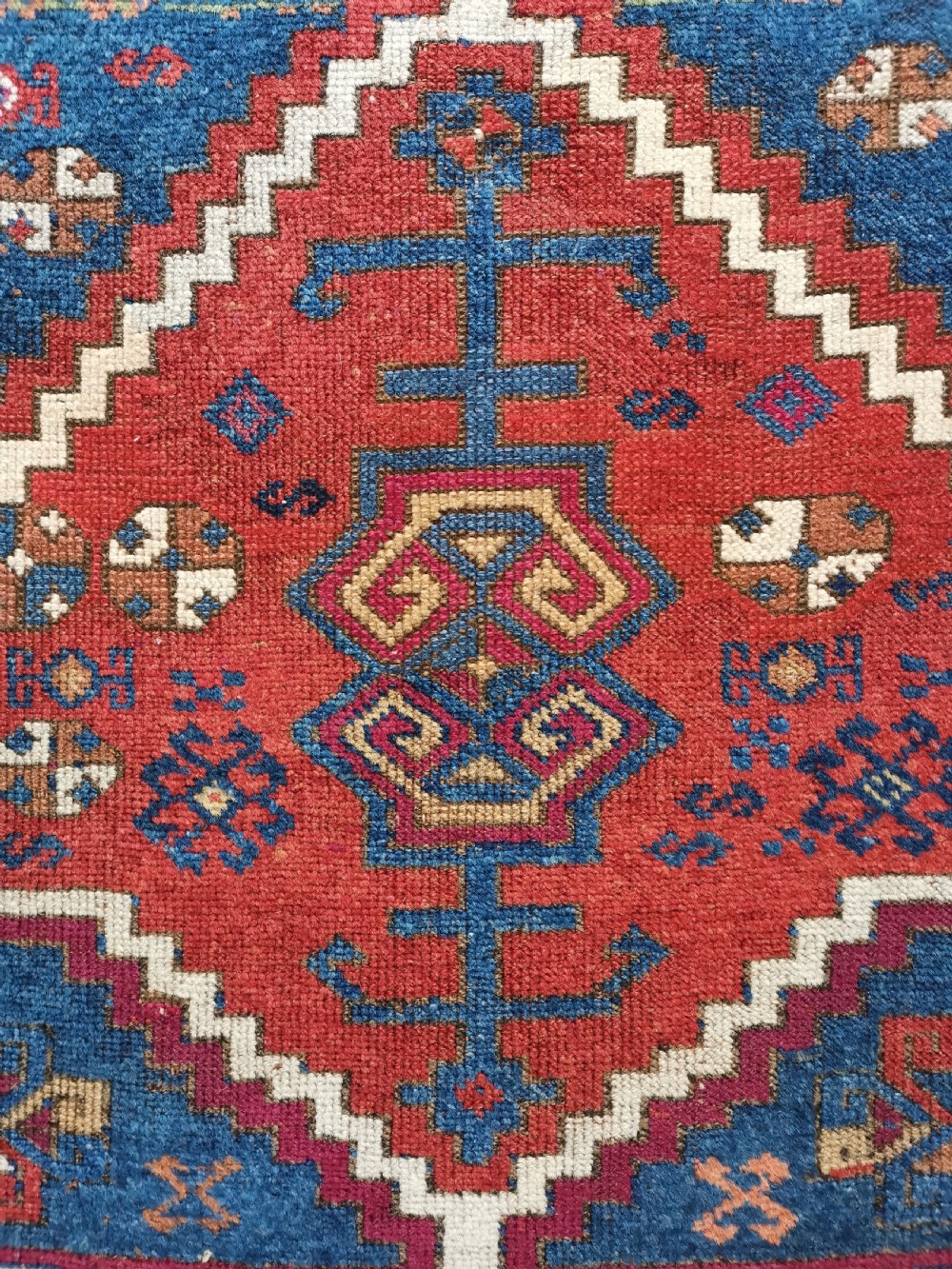 A rectangular hand-knotted wool rug featuring geometric stepped medallions and stylized tribal motifs in shades of red, indigo blue, terracotta, and off-white. View VIII